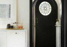 Black plank arch front door with a stained glass panel invites a vintage appeal to the foyer space.