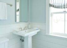 White and blue boys' bathroom features blue walls lined with white shiplap trim and holding a curved nickel mirror over a white pedestal sink with a polished nickel faucet kit. The washstand is fixed to gray mosaic marble floor tiles.