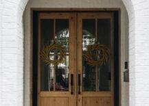 A white painted brick home features wood and glass double front doors accented with wreaths and oil rubbed bronze door handles.