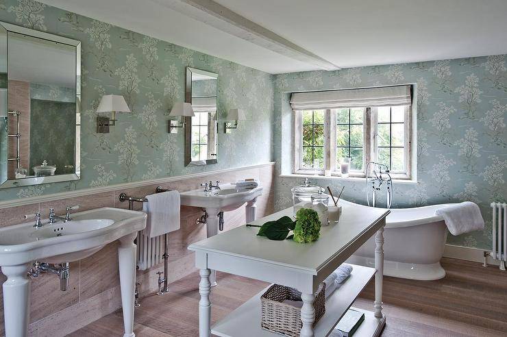 Blue French country bathroom features a pair of Parisian pedestal sinks and beveled mirrors flanking a radiator fitted with a towel warmer facing a white French island with turned legs. French master bathroom boasts a blue floral wallpaper lined with a spa tub and a vintage style tub filler.