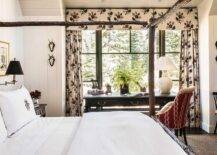 Elegant bedroom work space features a red desk chair placed at a black French desk topped with a white gourd lamp and positioned in front of windows dressed in floral curtains with a matching valance.