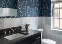 Gray marble offset wall tiles cover half of bathroom walls finished with Harlequin Salice Wallpaper, as a pivot mirror is mounted above a black washstand donning polished nickel pulls and a polished nickel faucet fixed to a black quartz countertop.