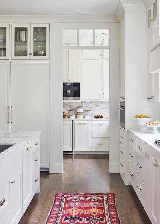 Colorful kitchen runner leads to a butler's pantry with a transom window and white cabinets with nickel pulls.