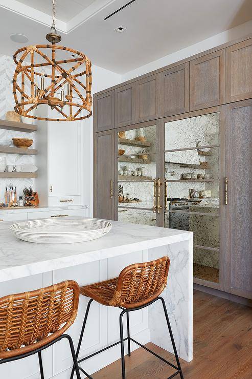 Rattan stools are placed at a marble waterfall edge island lit by bamboo drum shade lights.