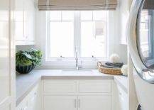 u shape small laundry room large natural light window tan roman shade stacked washer and dryer white shaker cabinets