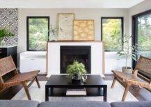 Mid century modern fireplace styled with two framed wall art pieces in a living room flanked by black framed windows and white built-in cabinets. A black coffee table furnishes the living space along with mid century modern chairs.