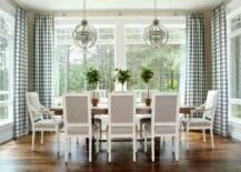 Chic dining room features a trestle dining table lined with heather gray square back French dining chairs illuminated by Restoration Hardware Victorian Hotel Pendants surrounded by windows dressed in blue gingham curtains.