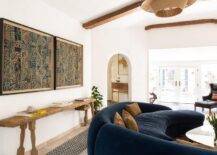 Vintage living room features reclaimed wood console table under framed fabric batik art and blue curved sofa with orange pillows.