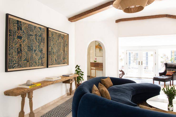 Vintage living room features reclaimed wood console table under framed fabric batik art and blue curved sofa with orange pillows.