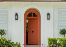 Bungalow features an orange front door illuminated by black lanterns.