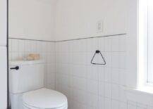 Half tiled vertical walls with black trim in a black and white bathroom boasting cement floor tiles under a vaulted ceiling.