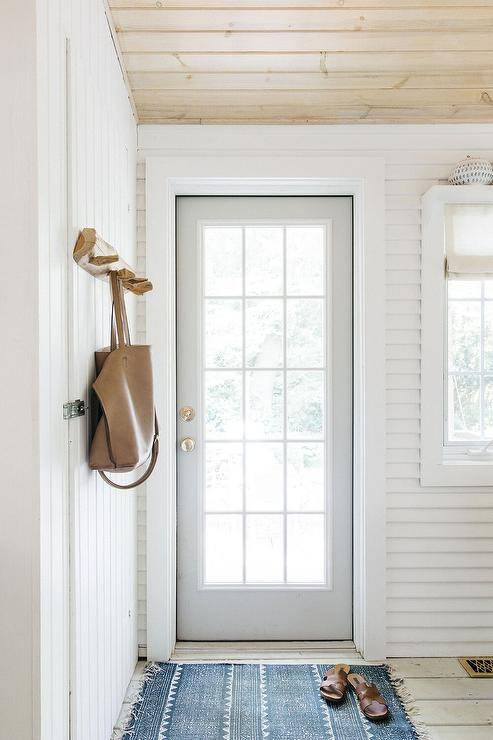 A blue vintage rug sits in an entryway beneath a blond plank ceiling and in front of a dove gray front door finished with 15 glass panels.