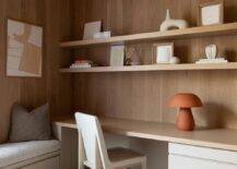 A wood and leather chair sits at a built in wooden desk illuminated by a terracotta mushroom lamp.