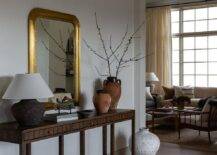 A gold leaf beaded mirror is mounted over a walnut console table with terracotta vases and a vintage runner.