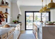 Eugene Pendants illuminate a white and tan kitchen island donning brass pulls and finished with a white quartz waterfall edge countertop.