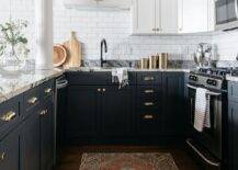 Black and white kitchen with two-toned cabinets and polished brass cup pulls boasting gray granite countertops and white subway tiles.