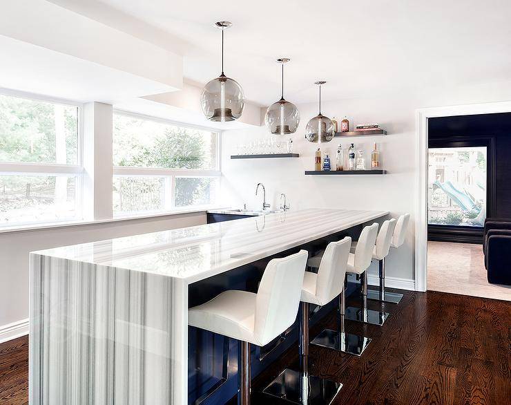 Smoke gray glass light pendants illuminate a modern blue kitchen island with a gray striped marble waterfall countertop and white swivel island stools.