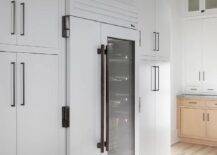 Black and white kitchen features a white modern fridge with a clear glass door and white cabinetry.