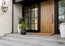 A welcome mat sits in front of a beige plant front door flanked by windows.