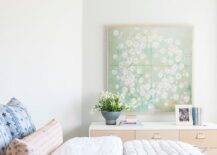 Green tapestry wall art above a two-tone dresser in a transitional bedroom completed with a white and gray bed and a gray silk quilt.