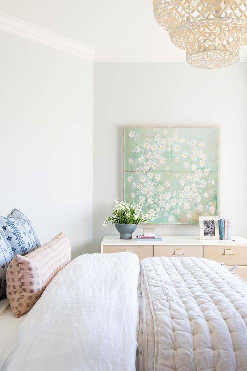 Green tapestry wall art above a two-tone dresser in a transitional bedroom completed with a white and gray bed and a gray silk quilt.