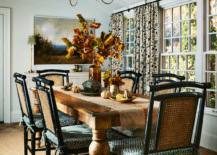 Dining room features black bamboo and cane dining chairs at a French dining table with turned legs lit by a brass Vendome chandelier hung from a vaulted plank ceiling and a tan rug.