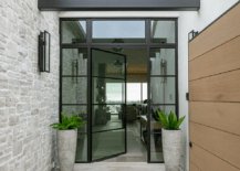 Cream travertine herringbone pattern pavers lead to a steel and glass front door flanked by sidelight and positioned beneath a transom window.