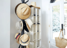 A black vintage metal baseball cap rack is placed in an entry boasting a white front door with a large glass panel and a matte black door handle and plate. The door is fixed beneath an arch transom window.