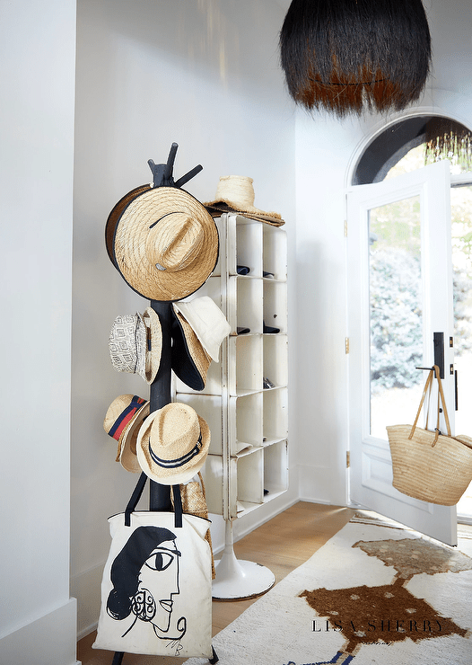 A black vintage metal baseball cap rack is placed in an entry boasting a white front door with a large glass panel and a matte black door handle and plate. The door is fixed beneath an arch transom window.