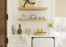 Stacked oak shelves are mounted over white kitchenette cabinets fitted in a bedroom and finished with a white mini Big Chill Fridge.